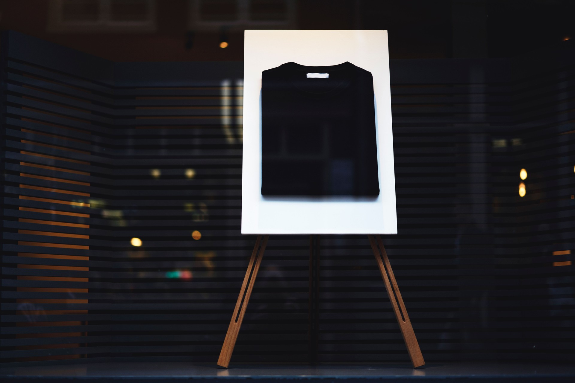 Stylish stand easel with a black basic casual folded t-shirt with mock up copy space area for your logo or brand name, display with clothing at the shop window storefront
