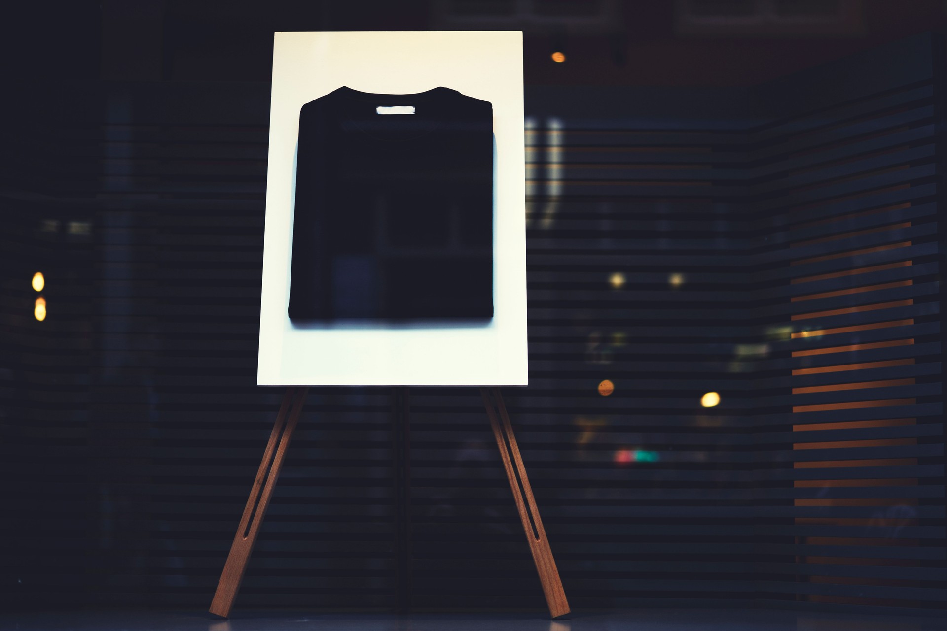 Stylish stand easel with a black basic casual folded t-shirt with mock up copy space area for your logo or brand name, display with clothing at the shop window storefront